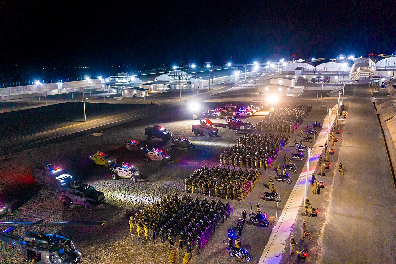 Night-time aerial view of security forces, armored vehicles, and helicopters assembled at the CECOT prison complex in El Salvador