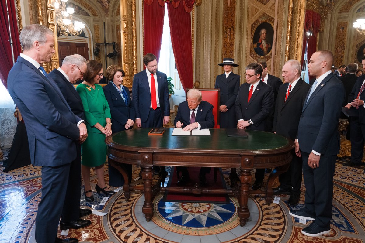President Trump signing documents at a desk in the U.S. Capitol on January 20, 2025, surrounded by congressional leaders